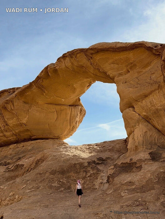Camel crossing Wadi Rum beneath a natural rock arch, Jordan